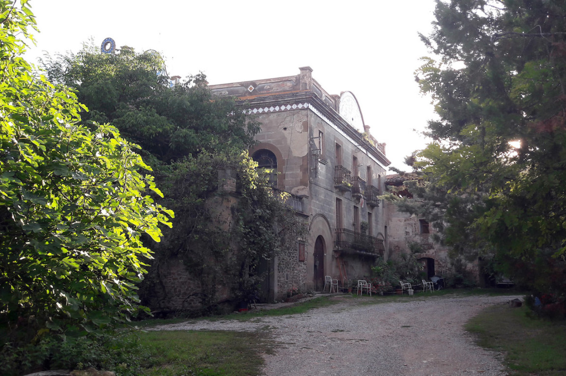 The photo shows the facade of the masía known as Can Rovira, which is in good structural condition, though it appears to need paint and some repairs.